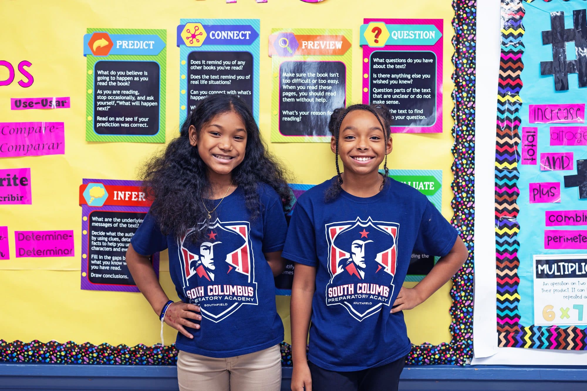 Two smiling students in South Columbus Preparatory Academy T-shirts in front of a reading bulletin board.
