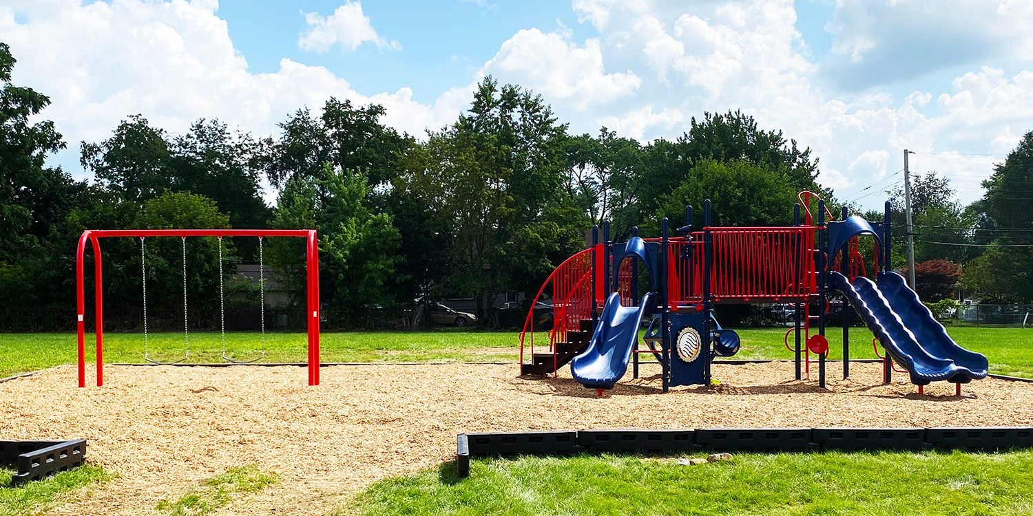 Empty playground with red swing set and blue and red slide structure.